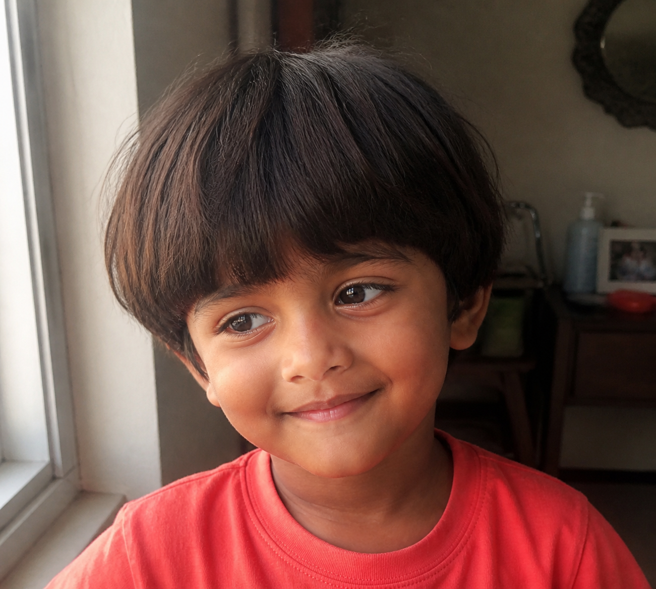 A candid headshot of five-year-old Arjun smiling softly by a window